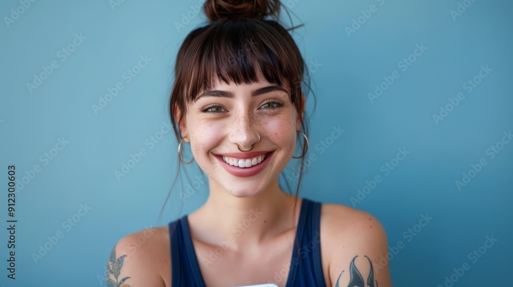 portrait of happy woman with smartphone, blue background, brunette hair in ponytail and bangs, tattoo on arm, smiling at camera portrait of happy woman with smartphone, blue background, brunette hair in ponytail and bangs, tattoo on arm, smiling at camera