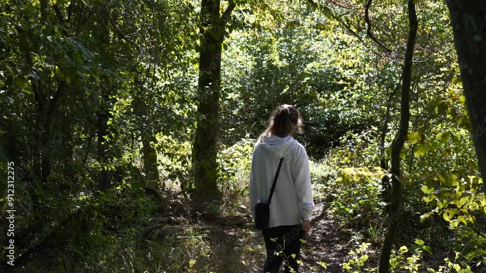 Woman walking alone in the forest, sun rays light up canopy, casual clothes Woman walking alone in the forest, sun rays light up canopy, casual clothes