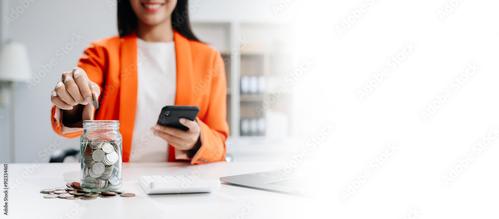 Saving money with hand putting coins in jug glass and calculator to calculate budget concept finance and accounting Saving money with hand putting coins in jug glass and calculator to calculate budget concept finance and accounting