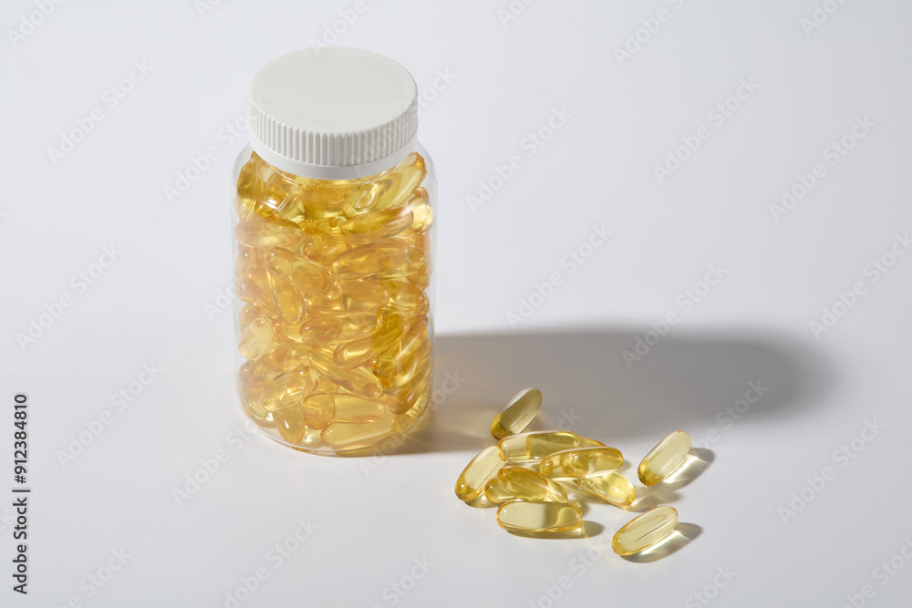White minimal background features an unbranded clear bottle full filled with yellow multivitamin capsules, which brings countless health benefits. Photo from high angle shot, advertising space White minimal background features an unbranded clear bottle full filled with yellow multivitamin capsules, which brings countless health benefits. Photo from high angle shot, advertising space