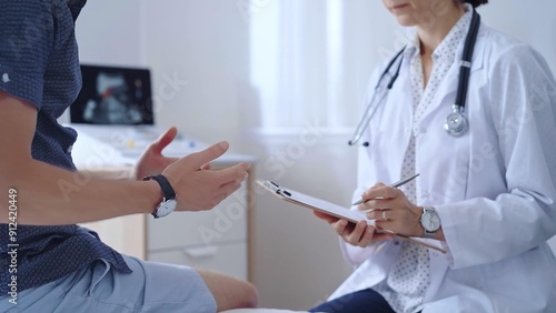 Doctor woman is taking notes on a clipboard while a male patient describes his symptoms in clinic procedure cabinet. Medicine service