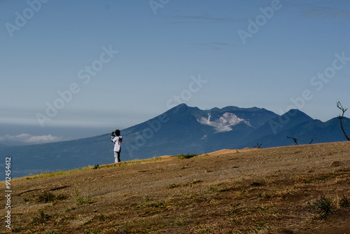 A climber wearing a white shirt is taking photos of the scenic landscape with the Papandayan mountains in the background, like in Europe photo