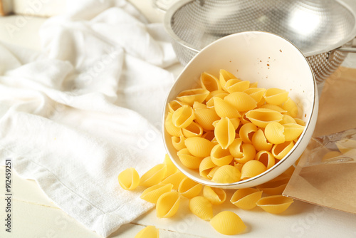 Bowl with raw conchiglie pasta on light wooden background photo