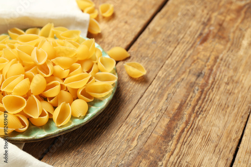 Plate with raw conchiglie pasta on wooden background, closeup photo