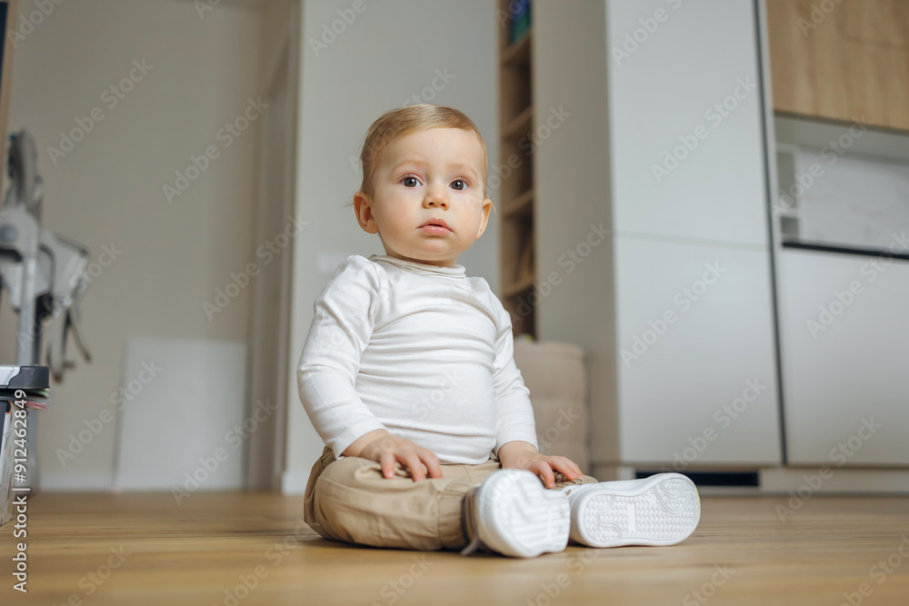 Adorable Baby in White Shirt Sitting on Floor in Modern Home Adorable Baby in White Shirt Sitting on Floor in Modern Home
