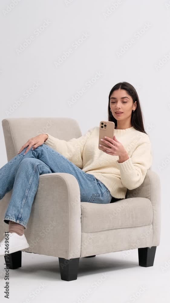 Smiling Caucasian young adult woman greeting during online video call and chatting with friends using phone on white background. Vertical video. Smiling Caucasian young adult woman greeting during online video call and chatting with friends using phone on white background. Vertical video.