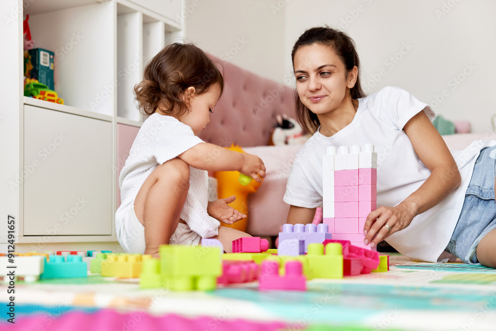 cute baby girl and her loving mother playing with toy bricks in the children room, having fun together cute baby girl and her loving mother playing with toy bricks in the children room, having fun together