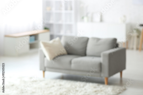 Interior of light living room with grey sofa  chest of drawers and carpet  blurred view