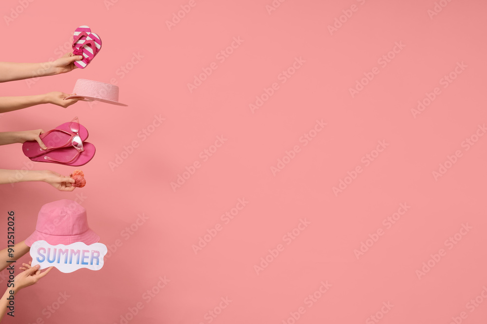 Hands holding pair of flip flops with beach accessories and paper with word SUMMER on pink background Hands holding pair of flip flops with beach accessories and paper with word SUMMER on pink background