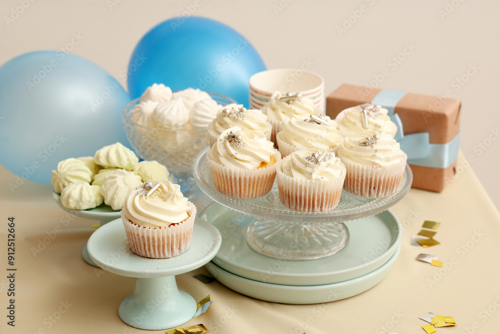 Dessert stands with tasty white cupcakes, decor and other sweets for birthday party on table