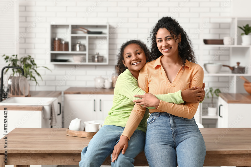 Beautiful young happy African-American mother with her daughter hugging in kitchen at home Beautiful young happy African-American mother with her daughter hugging in kitchen at home