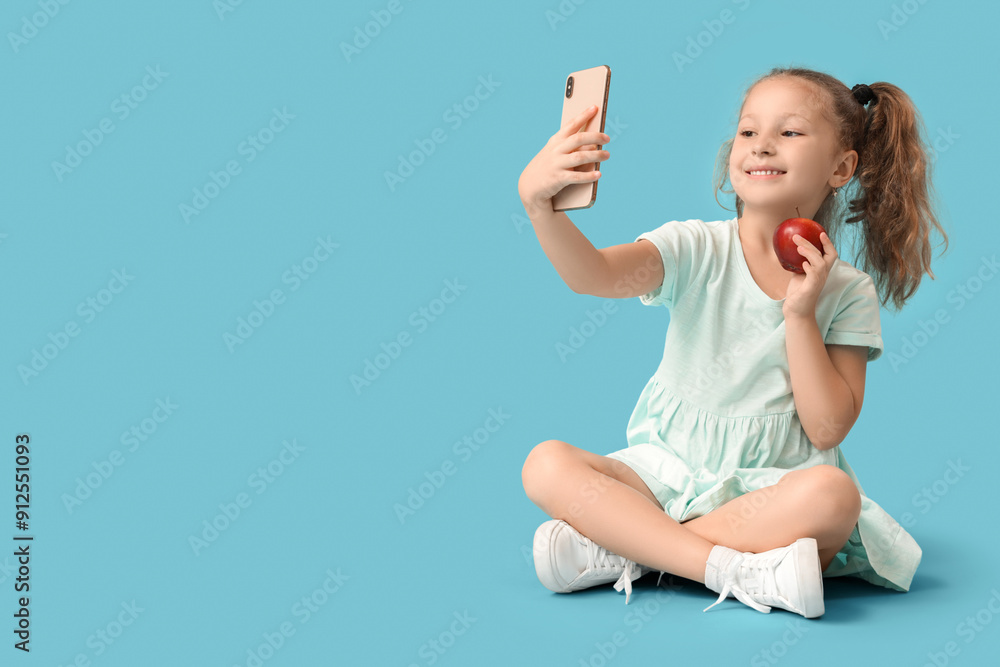 Cute little girl with red apple taking selfie on blue background Cute little girl with red apple taking selfie on blue background