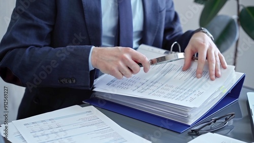 Adult businessman or auditor examining documents with magnifying glass. Professional in a suit scrutinizes financial reports, detail-focused work concept