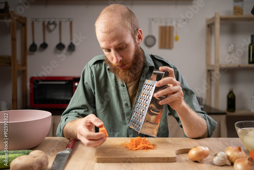 Canvas Print man grating fresh ripe carrot at wooden table in his home kitchen