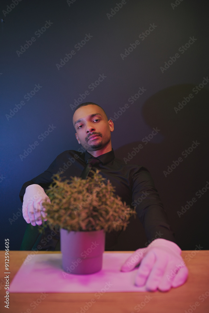 African American middle-aged man with short dark hair, wearing a black shirt and carrying a bouquet of flowers, plants on a dark blue background. African American middle-aged man with short dark hair, wearing a black shirt and carrying a bouquet of flowers, plants on a dark blue background.