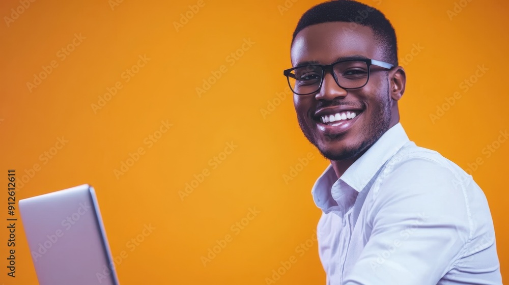 Cheerful Young Man with Glasses Working on Laptop Against Orange Background Cheerful Young Man with Glasses Working on Laptop Against Orange Background