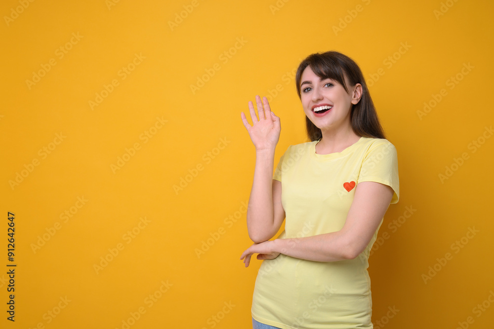 Happy young woman waving on orange background, space for text Happy young woman waving on orange background, space for text