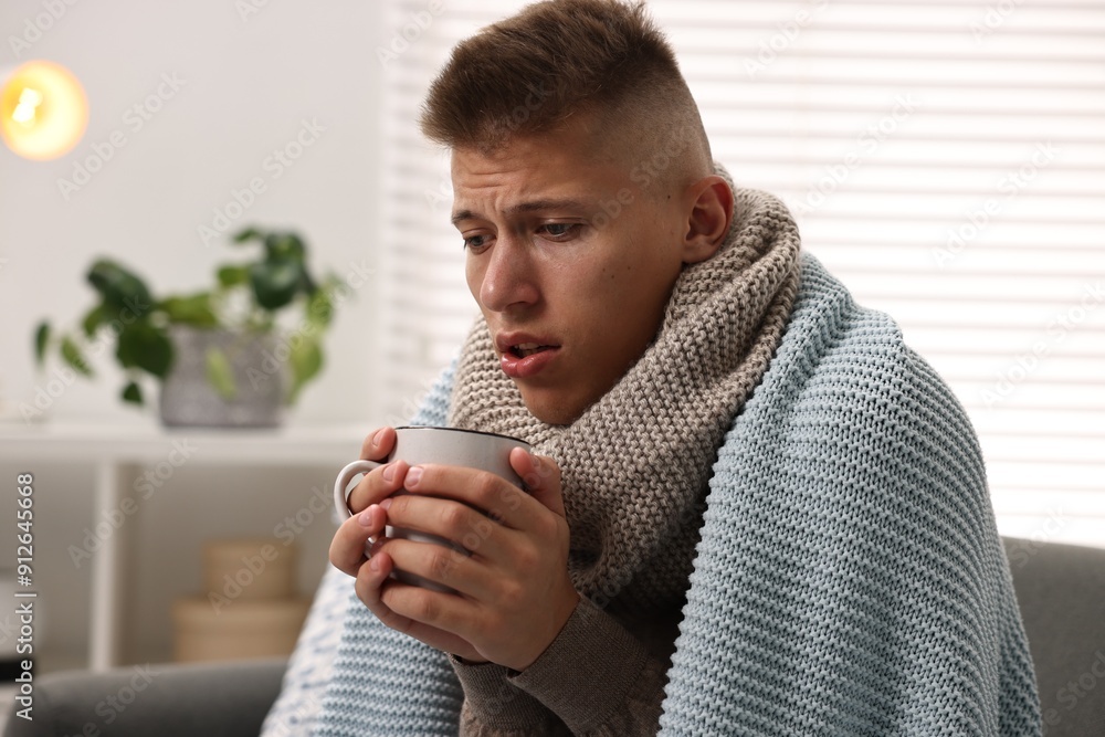 Cold symptom. Young man with hot tea suffering from fever at home Cold symptom. Young man with hot tea suffering from fever at home