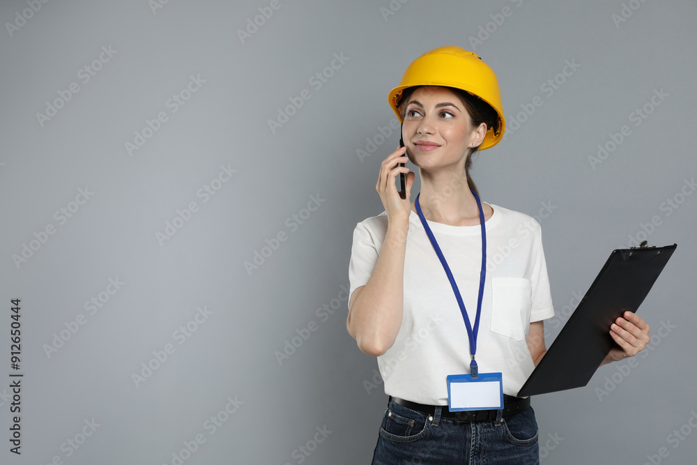 Engineer in hard hat with clipboard talking on smartphone against grey background, space for text Engineer in hard hat with clipboard talking on smartphone against grey background, space for text