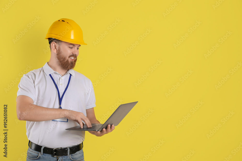 Engineer in hard hat with laptop on yellow background, space for text Engineer in hard hat with laptop on yellow background, space for text