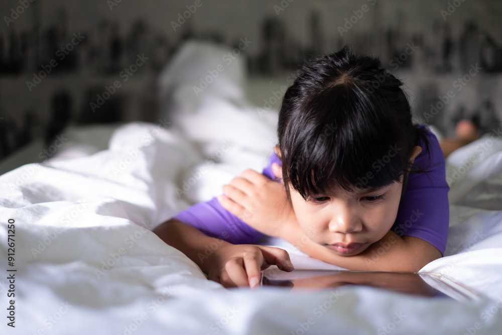 Cute Asian girl, 5-6 years old, sitting and playing with a tablet on a soft white mattress, online education learning technology, early childhood education, internet learning. Cute Asian girl, 5-6 years old, sitting and playing with a tablet on a soft white mattress, online education learning technology, early childhood education, internet learning.