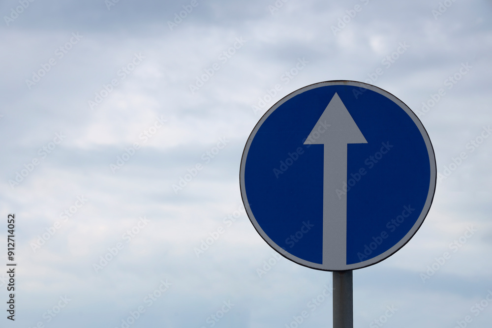 Circle road sign with directly white arrow on blue cloudy sky heaven background. empty copy space for inscription. Circle road sign with directly white arrow on blue cloudy sky heaven background. empty copy space for inscription.