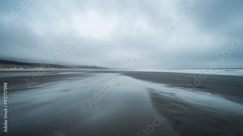 A tranquil beach lies empty under a gray sky, reflecting autumn's chill in the wet sand, inviting solitude and contemplation