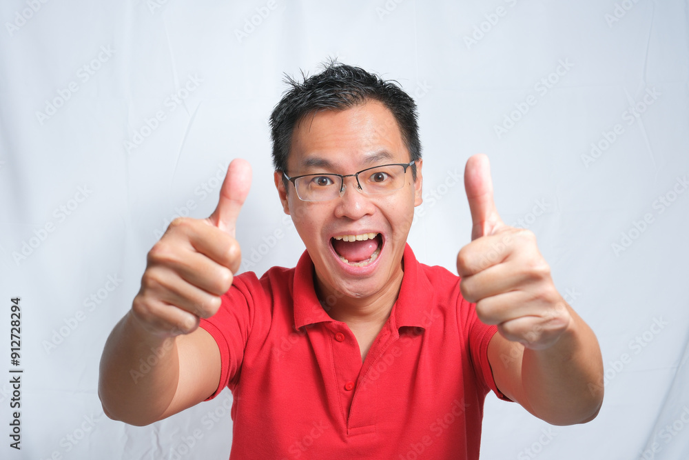 Portrait of young handsome asian man wearing red shirt and glasses posing against white isolated background. Make two thumbs up gesture and looks so happy. Portrait of young handsome asian man wearing red shirt and glasses posing against white isolated background. Make two thumbs up gesture and looks so happy.