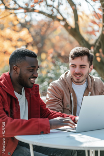 a young African-American man and a young white man working together on a computer at a table outdoors 