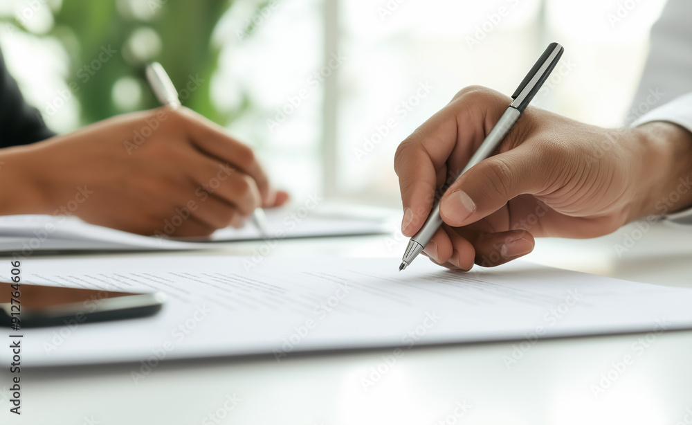 Two people signing documents together at a desk, focused on their hands. Two people signing documents together at a desk, focused on their hands.