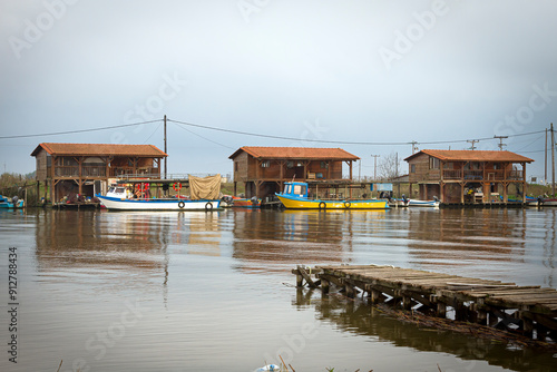 Tranquil afternoon at Delta Aliakmona, Greece, featuring rustic fishing huts and a weathered wooden pier extending into calm waters photo