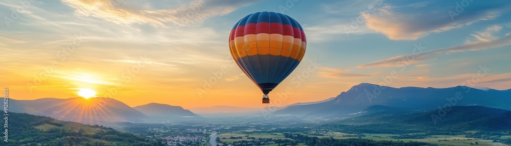 Fototapeta premium Hot air balloon flying over green valley with road and mountain