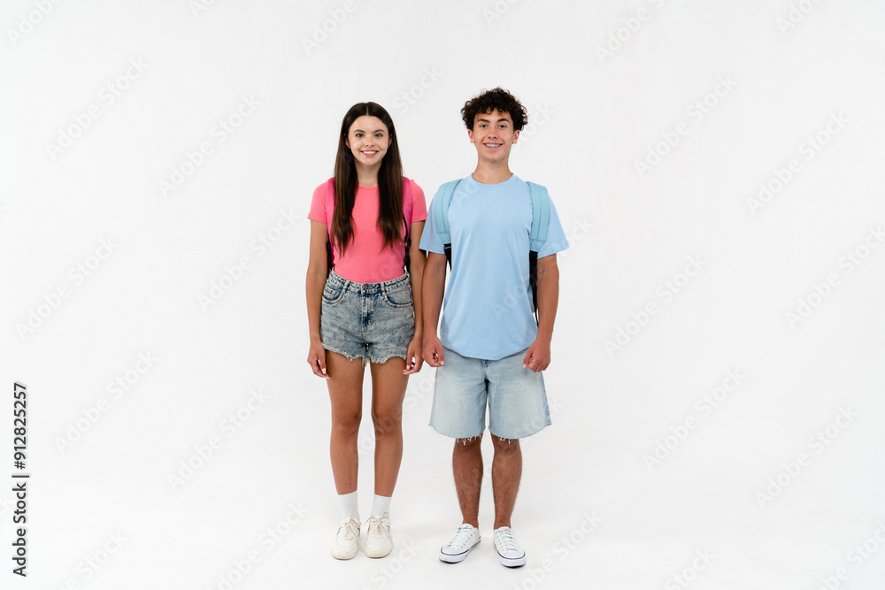 Full length of high school pupils students teenagers classmates boy and girl in casual clothes with bag standing posing looking at camera isolated on white background. Education back to school concept Full length of high school pupils students teenagers classmates boy and girl in casual clothes with bag standing posing looking at camera isolated on white background. Education back to school concept