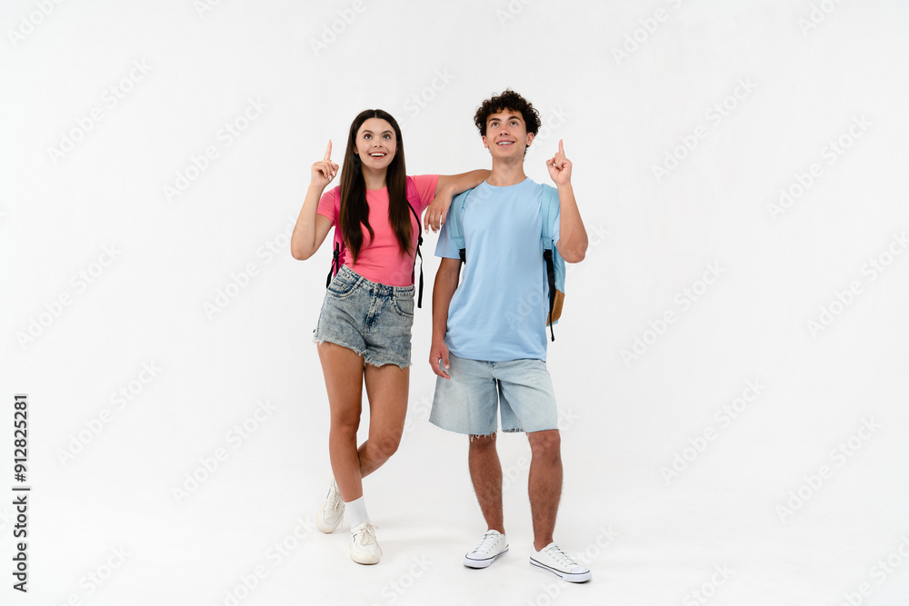 Full length of high school pupils students teenagers classmates boy girl friends in casual with bags looking pointing index finger up isolated on white background. Education advertisement concept Full length of high school pupils students teenagers classmates boy girl friends in casual with bags looking pointing index finger up isolated on white background. Education advertisement concept