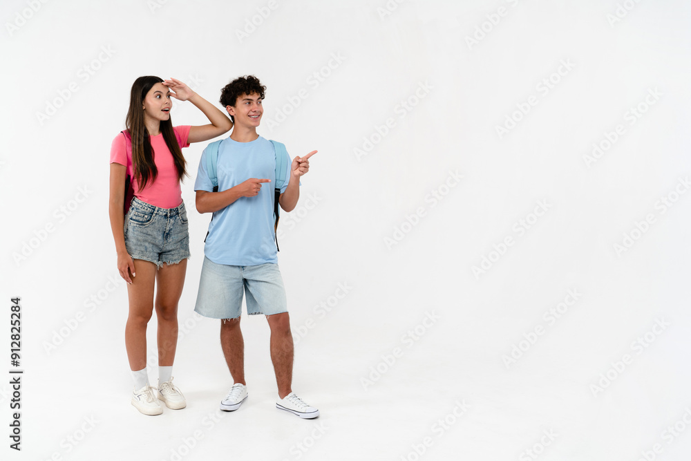 Full length of surprised high school pupils students teenagers classmates boy girl friends in casual with bags looking pointing at empty copy space blank isolated white background. Education concept Full length of surprised high school pupils students teenagers classmates boy girl friends in casual with bags looking pointing at empty copy space blank isolated white background. Education concept