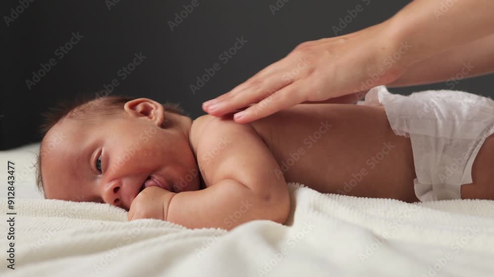 Doctor performing gentle therapy on cute baby infant resting on bed anonymous mother massaging her baby's back for relaxation, care and muscles development Doctor performing gentle therapy on cute baby infant resting on bed anonymous mother massaging her baby's back for relaxation, care and muscles development