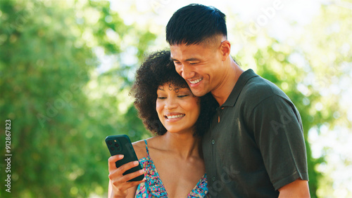 Young Couple Enjoying Time Together While Using a Smartphone in a Park on a Sunny Day