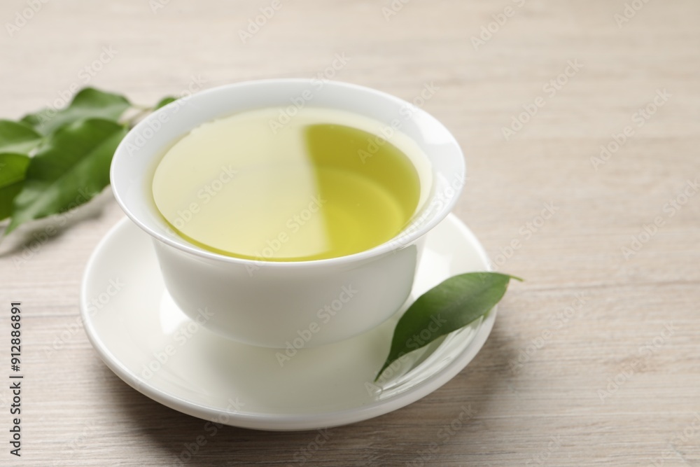 Refreshing green tea in cup and leaves on wooden table, closeup Refreshing green tea in cup and leaves on wooden table, closeup
