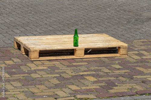 green beer bottle stands outside on a wooden pallet on the street photo