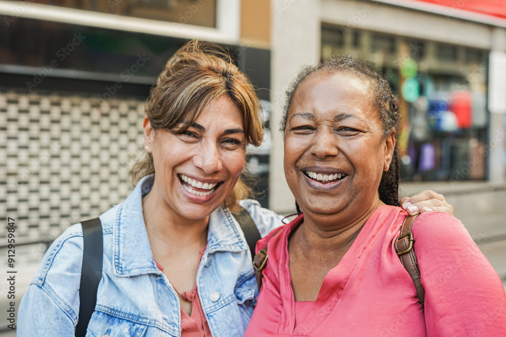 Happy multiracial female friends having fun smiling in front of camera during travel vacation in the city - Mature people hugging each other outdoor - Focus on the african woman face Happy multiracial female friends having fun smiling in front of camera during travel vacation in the city - Mature people hugging each other outdoor - Focus on the african woman face
