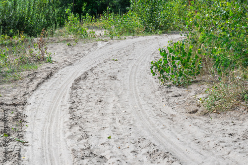 Sand road in the forest. Tire pattern of quad bike on driveway. Track imprint of quadricycle on nature land. Sand texture off road. Path in forest close up. Sand mounds and green forest in sunny day.
