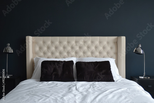 An elegant bedroom featuring a tufted beige headboard and dual modern metallic lamps on either side of the bed, with a bold, dark accent wall creating contrast. photo