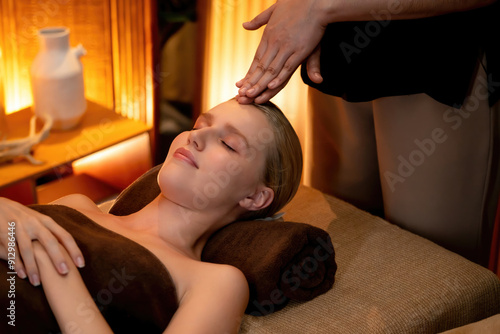 Caucasian woman enjoying relaxing anti-stress head massage and pampering facial beauty skin recreation leisure in warm candle lighting ambient salon spa in luxury resort or hotel. Quiescent