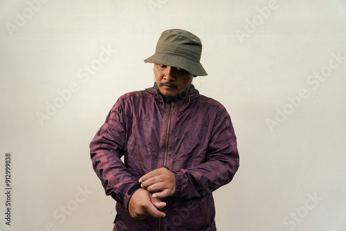 Half body portrait of adult Asian man with beard and mustache posing in various styles. Mature man wearing adventure outfit with jacket and bucket hat isolated on beige background.