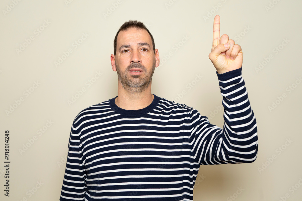 Bearded hispanic man about 40s wearing casual clothes posing isolated over beige background. People sincere emotions lifestyle concept. Copy space mockup. Pointing index finger up. Bearded hispanic man about 40s wearing casual clothes posing isolated over beige background. People sincere emotions lifestyle concept. Copy space mockup. Pointing index finger up.