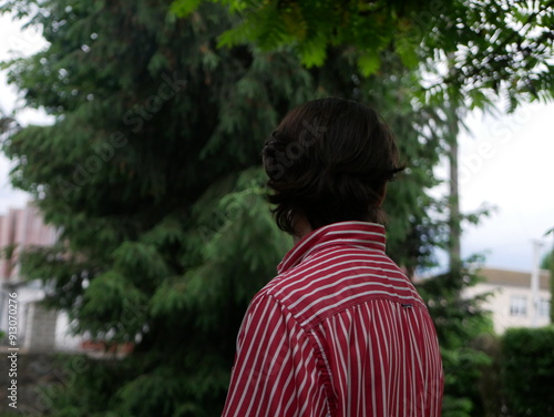 A man in a striped shirt looks mysteriously against the background of trees