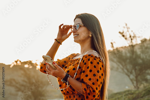 Beautiful brunette girl close-up shot smiling using her cell phone at the beach by sunset