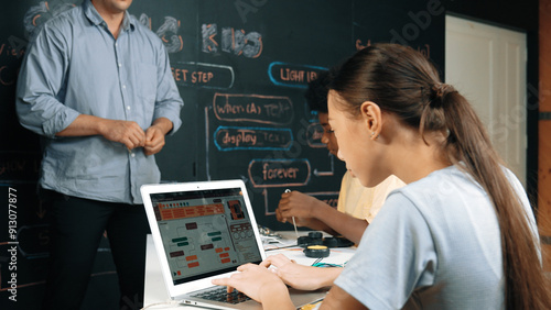 Teacher teaching about coding system while diverse academic student fixing main board at table with laptop display programing prompt or engineering code at STEM technology classroom. Edification.