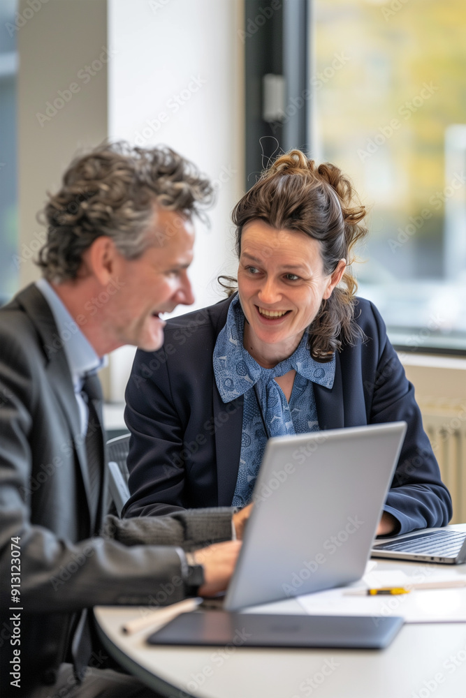 Close up of a cheerful middle-aged businessman conversing with a businesswoman at a desk in a meeting room. Close up of a cheerful middle-aged businessman conversing with a businesswoman at a desk in a meeting room.