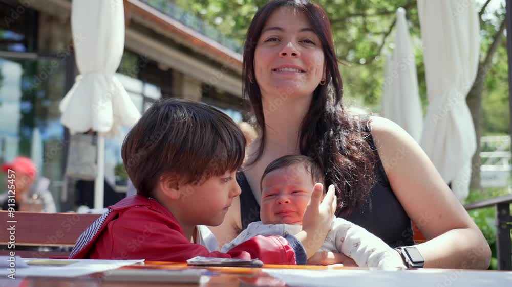 Mother with her two children, an older sibling hugging a newborn baby while sitting at an outdoor cafe, highlighting the joy of family bonding and the welcoming of a new family member Mother with her two children, an older sibling hugging a newborn baby while sitting at an outdoor cafe, highlighting the joy of family bonding and the welcoming of a new family member